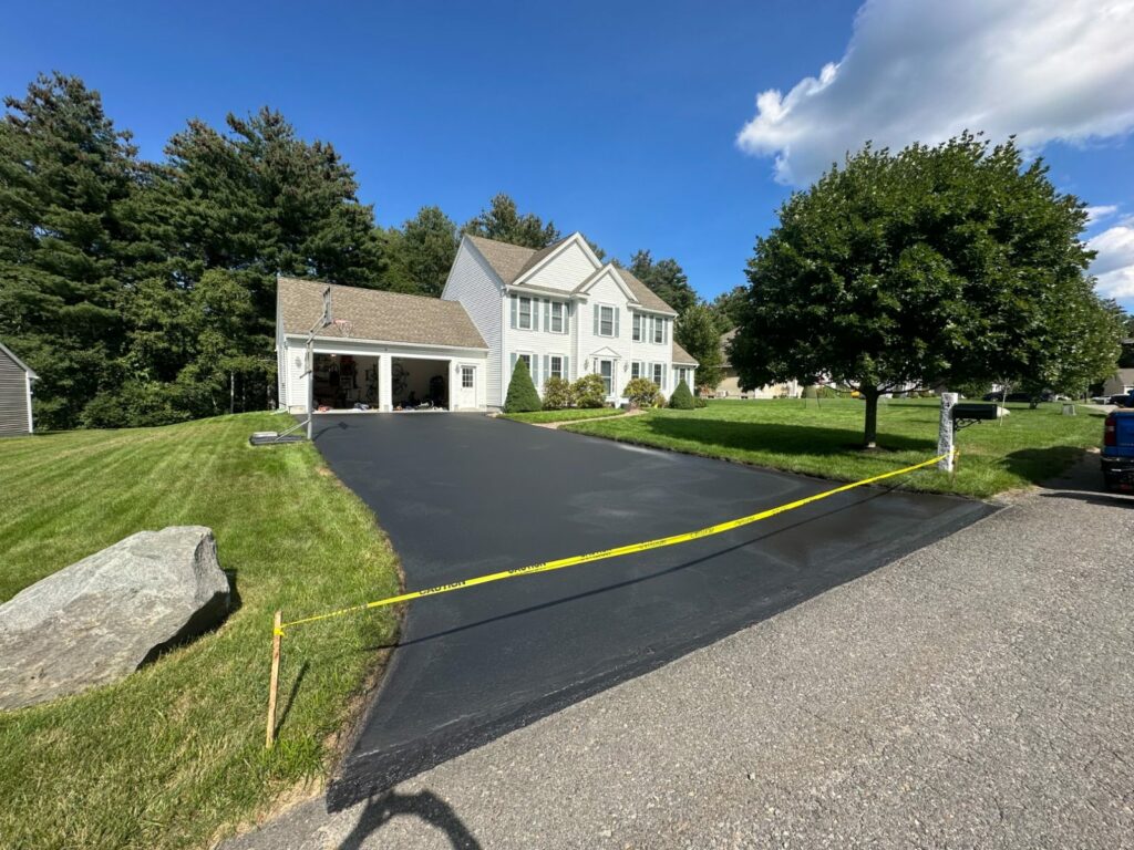 Freshly sealcoated driveway apron with caution tape, a boulder and a granite mailbox post in Littleton, MA.