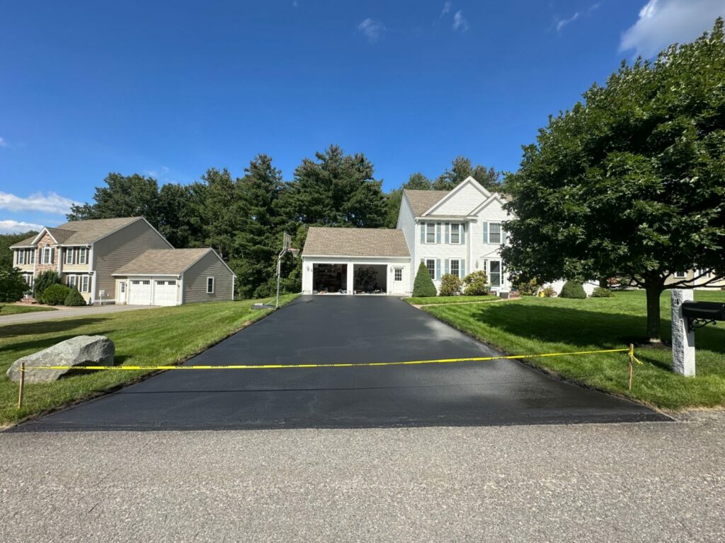 Wide, freshly sealcoated driveway leading to an attached two-car garage at a colonial home in Littleton, MA.